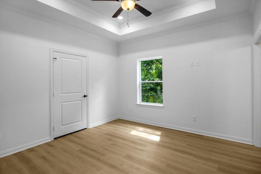 Unfurnished room featuring a tray ceiling, light wood-type flooring, a ceiling fan, ornamental molding, and recessed lighting