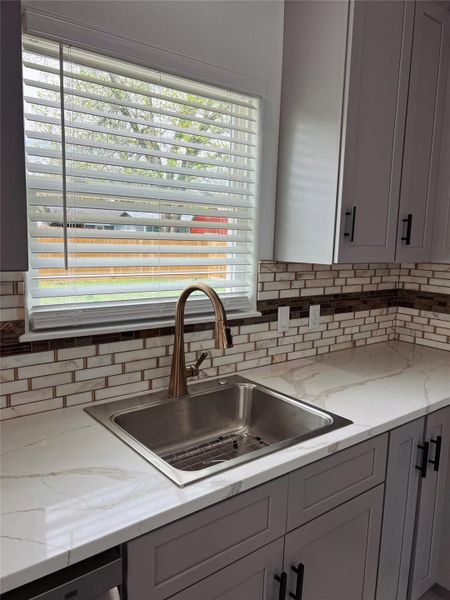 Kitchen with decorative backsplash, light stone countertops, and a sink Kitchen with decorative backsplash, light stone countertops, and a sink