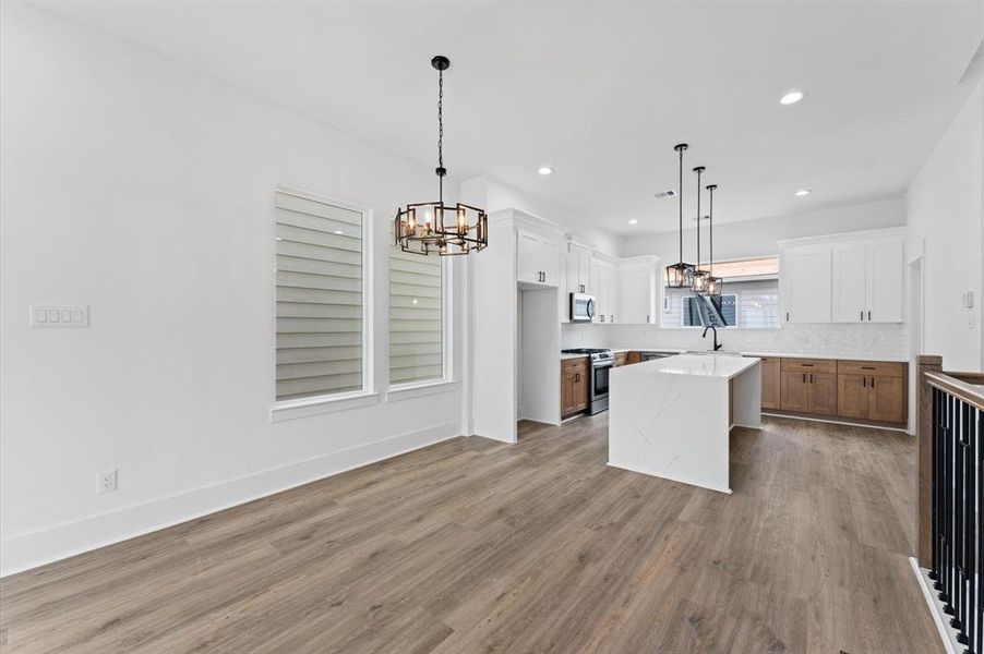 This photo showcases a modern open-concept kitchen and dining area with elegant light fixtures. The kitchen features a large island, white cabinets, and stainless steel appliances, complemented by wood flooring and ample natural light.