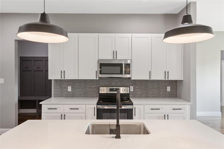 Kitchen with white cabinets, stainless steel appliances, tasteful backsplash, and decorative light fixtures