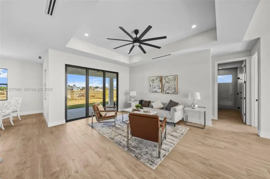 Tray ceiling featuring a multi-blade ceiling fan, wood-finish flooring, recessed lighting, and expansive multi-panel sliding glass doors Tray ceiling featuring a multi-blade ceiling fan, wood-finish flooring, recessed lighting, and expansive multi-panel sliding glass doors