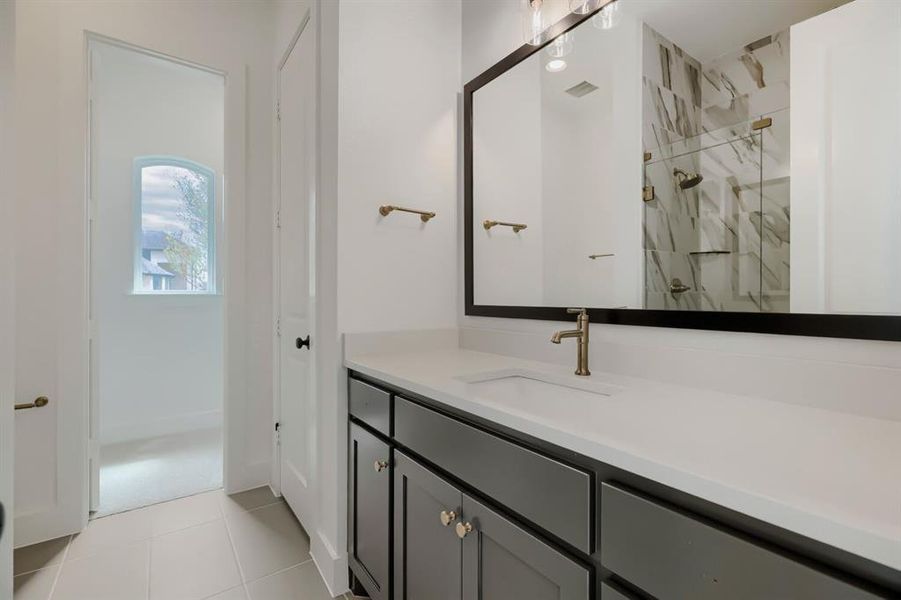 Bathroom featuring a gray vanity with a light-toned countertop, a large framed mirror, and a walk-in shower with large format tile Bathroom featuring a gray vanity with a light-toned countertop, a large framed mirror, and a walk-in shower with large format tile
