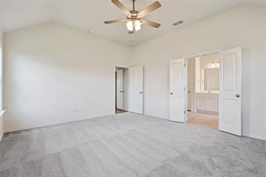 Unfurnished bedroom with ensuite bath, vaulted ceiling, light colored carpet, and ceiling fan