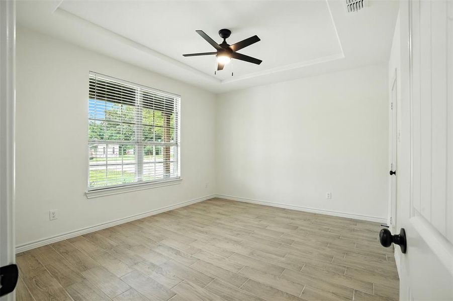 Empty room with a tray ceiling, light wood finished floors, and ceiling fan