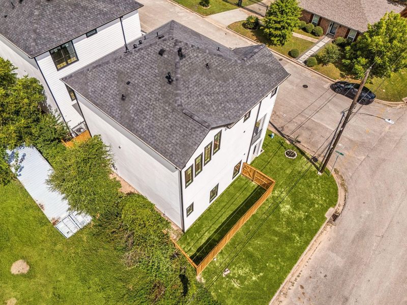 A beautiful aerial view from behind the home highlights the property's exterior, corner lot setting, and surrounding views beneath blue skies.
