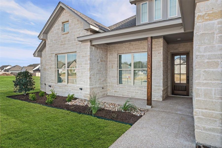 View of exterior entry featuring a yard, covered porch, and stone siding
