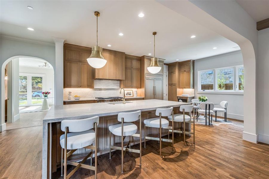 Kitchen with arched walkways, light stone countertops, ornamental molding, a breakfast bar area, and a large island Kitchen with arched walkways, light stone countertops, ornamental molding, a breakfast bar area, and a large island