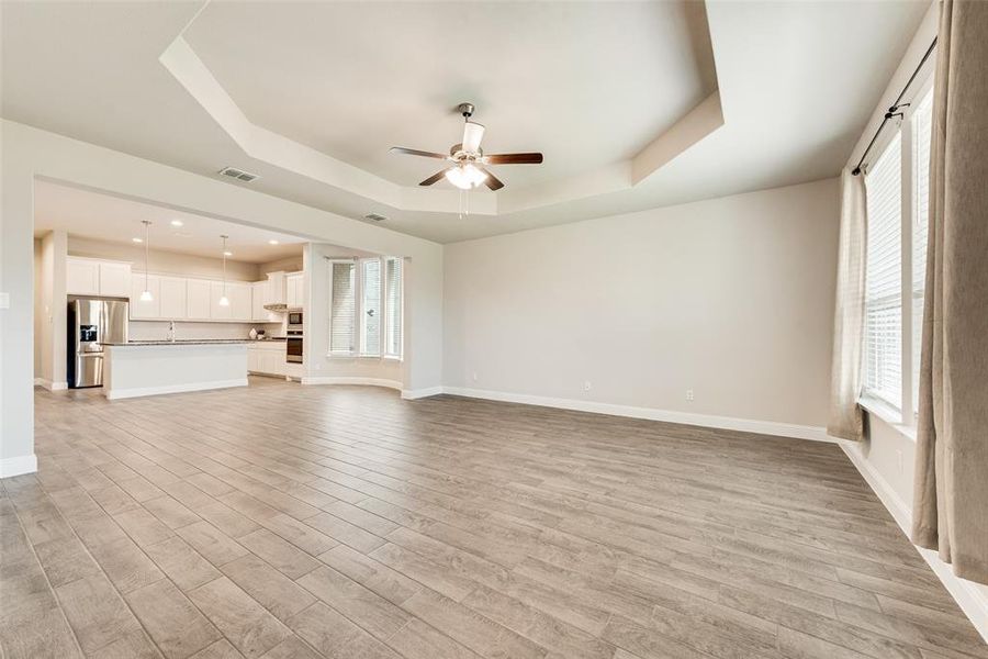Unfurnished living room with a tray ceiling, ceiling fan, and healthy amount of natural light