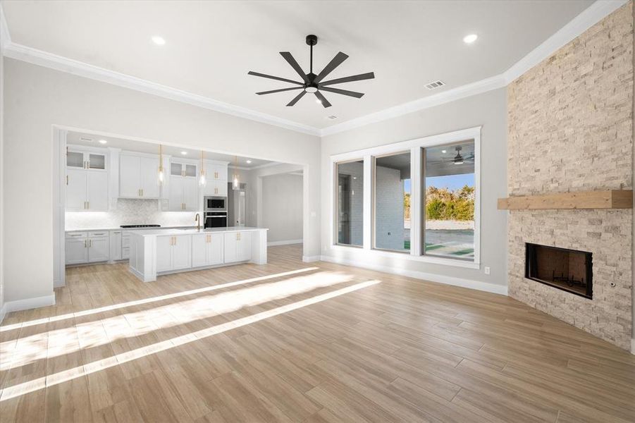 Unfurnished living room featuring ceiling fan, crown molding, sink, light hardwood / wood-style flooring, and a fireplace