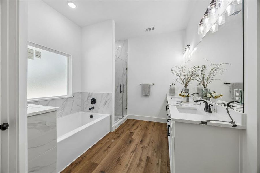 Primary ensuite bathroom featuring a large tub and a shower with frameless glass