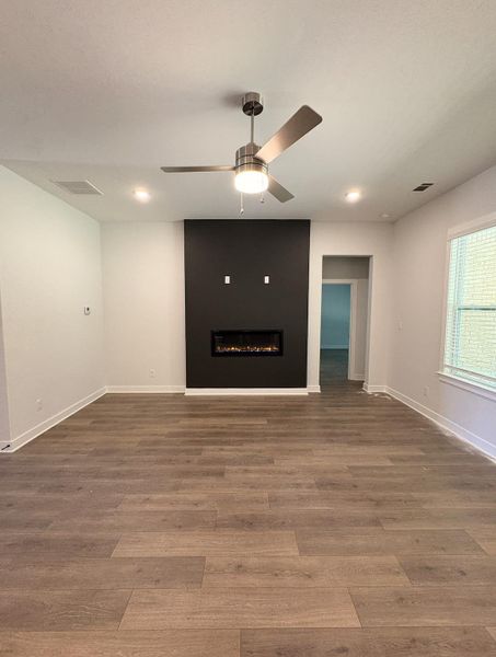 Wood-finish flooring, recessed lighting, ceiling fan with light fixture, and an electric fireplace set into a dark accent wall