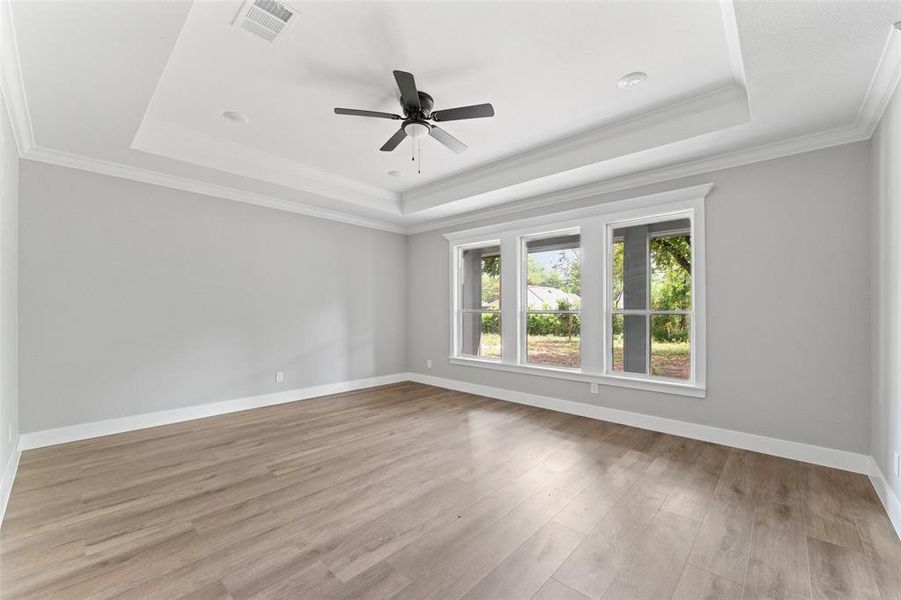 Empty room featuring a raised ceiling, ornamental molding, light wood-style flooring, and ceiling fan