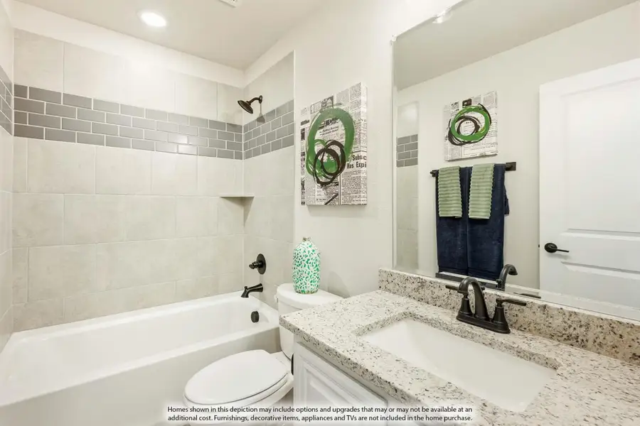 Bathroom with granite countertop vanity, white soaking tub, and tiled shower with gray accent tiles