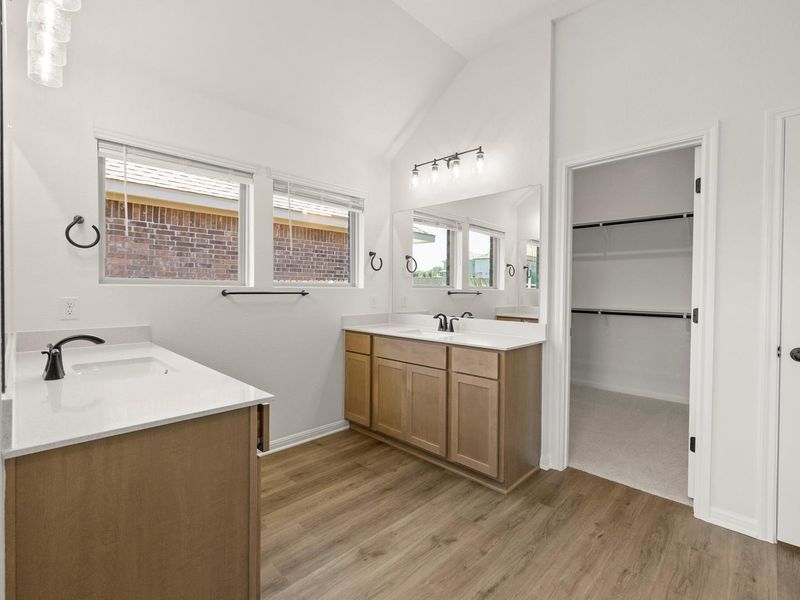 Bathroom featuring dual vanity sinks with light wood-finish cabinetry, white countertops, and black hardware