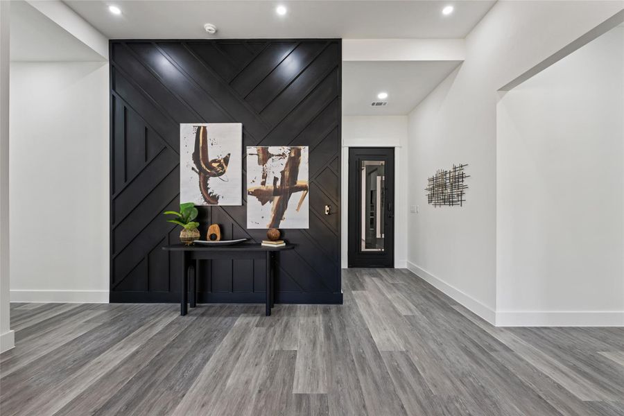 Entryway featuring a striking black accent wall with geometric paneling, recessed lighting, and light wood-finish flooring