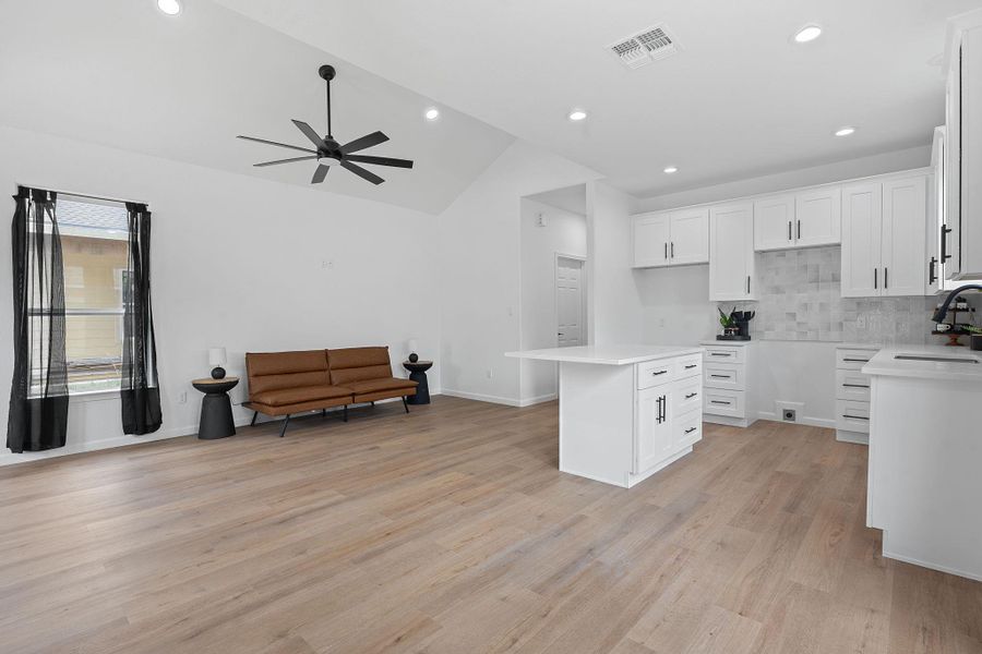 Kitchen featuring vaulted ceiling, ceiling fan, light wood-style floors, tasteful backsplash, and white cabinetry