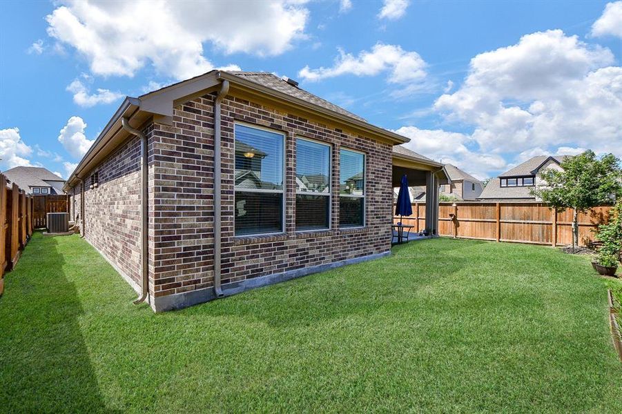 This photo shows a well-maintained brick home with a spacious, fenced backyard. The lawn is lush and green, and there's a covered patio area for outdoor relaxation. A great space for family activities or entertaining guests.