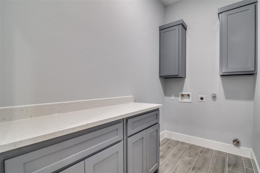 Washroom with hookup for an electric dryer, hookup for a washing machine, light wood-type flooring, and cabinets