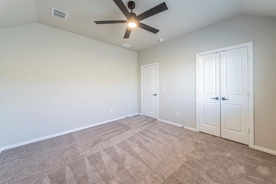 Spacious room featuring vaulted ceilings, a contemporary ceiling fan, light gray wall paint, and plush gray carpet flooring