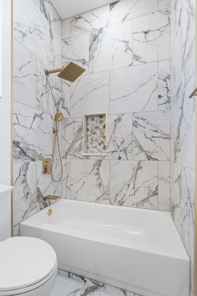 Marble-look tile and gold fixtures complete this pristine bathroom space. Marble-look tile and gold fixtures complete this pristine bathroom space.