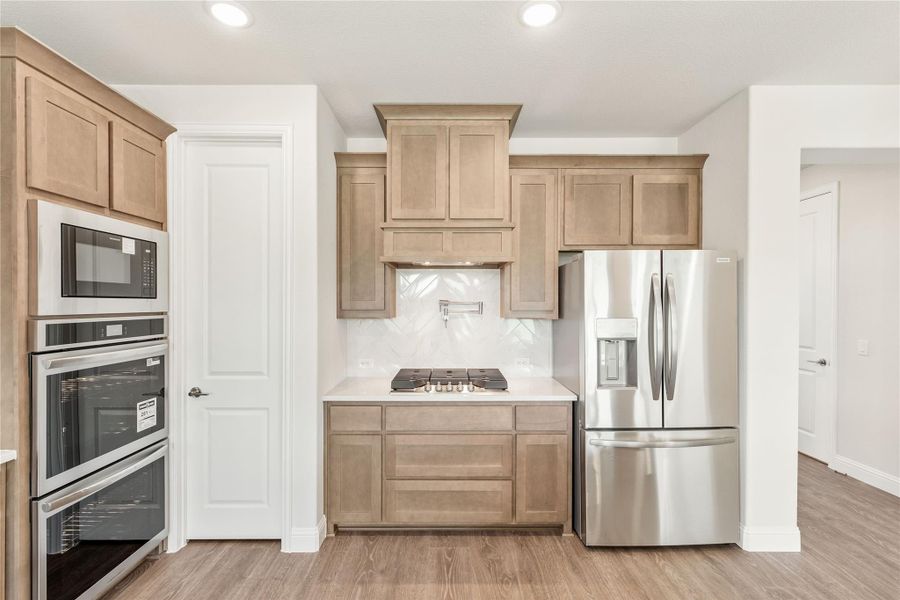 Kitchen with tan wood cabinets, stainless steel appliances, gas cooktop, and herringbone tile backsplash