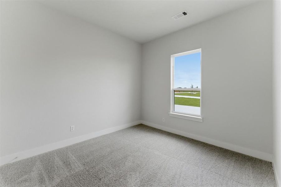 Room with light gray walls, gray carpet, white baseboards, and a single window with white trim, featuring an exterior view of a green landscape under a blue sky