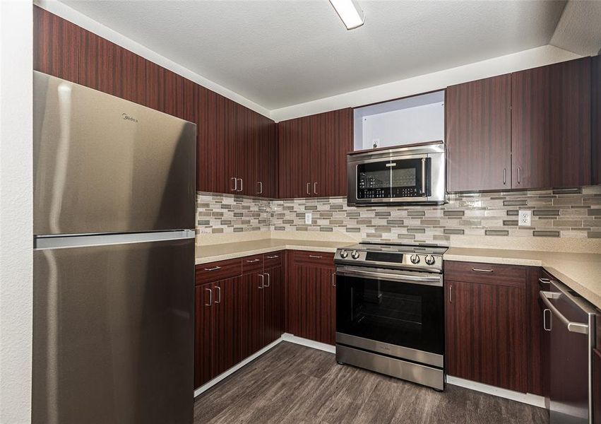 Kitchen featuring appliances with stainless steel finishes, designer backsplash, and luxury vinyl wood-type flooring