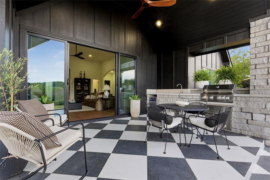 Covered outdoor patio featuring a black and white checkerboard floor, built-in stone grill station with integrated sink, and expansive glass sliding doors
