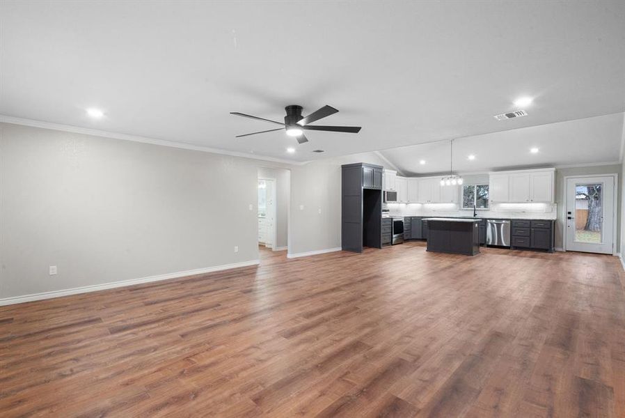 Unfurnished living room with crown molding, ceiling fan with notable chandelier, vaulted ceiling, and hardwood / wood-style flooring Unfurnished living room with crown molding, ceiling fan with notable chandelier, vaulted ceiling, and hardwood / wood-style flooring