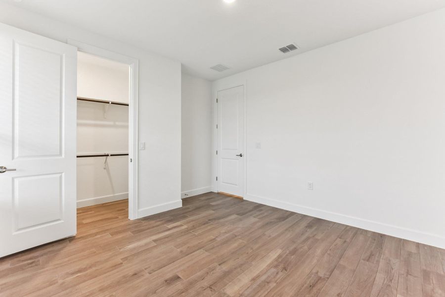 Unfurnished bedroom with a spacious closet and light wood finished floors Unfurnished bedroom with a spacious closet and light wood finished floors