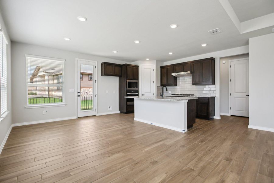 Kitchen featuring tasteful backsplash, dark brown cabinetry, recessed lighting, light stone counters, and a center island with sink Kitchen featuring tasteful backsplash, dark brown cabinetry, recessed lighting, light stone counters, and a center island with sink