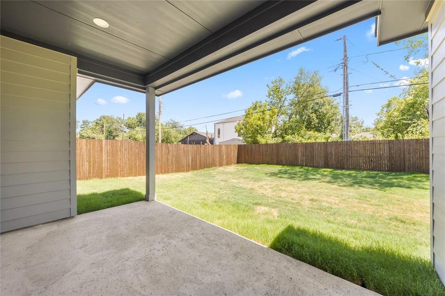 Covered patio with a concrete surface, providing exterior access to a grassy yard enclosed by a wooden privacy fence