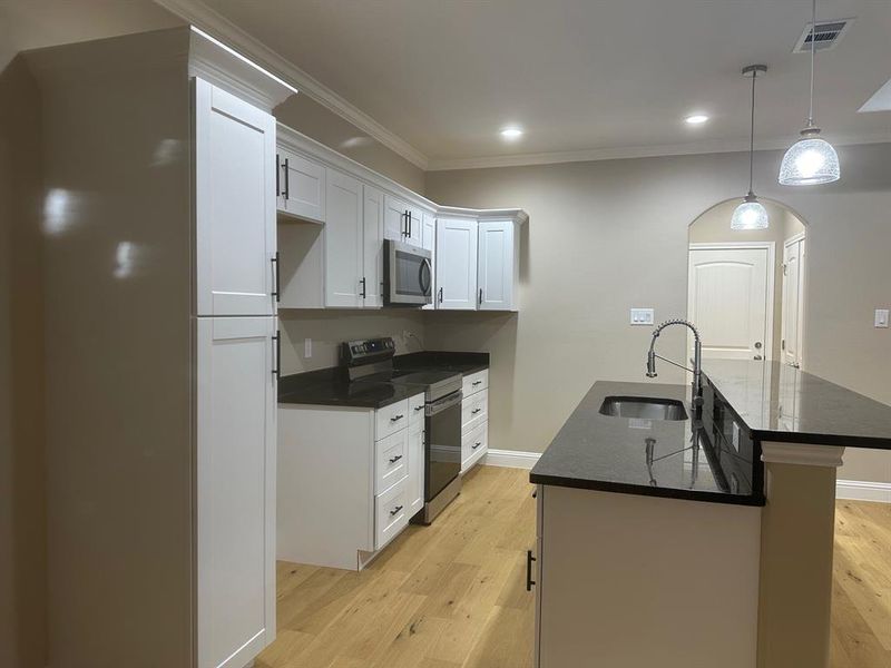 Kitchen featuring an island with sink, sink, white cabinetry, stainless steel appliances, and light wood-type flooring