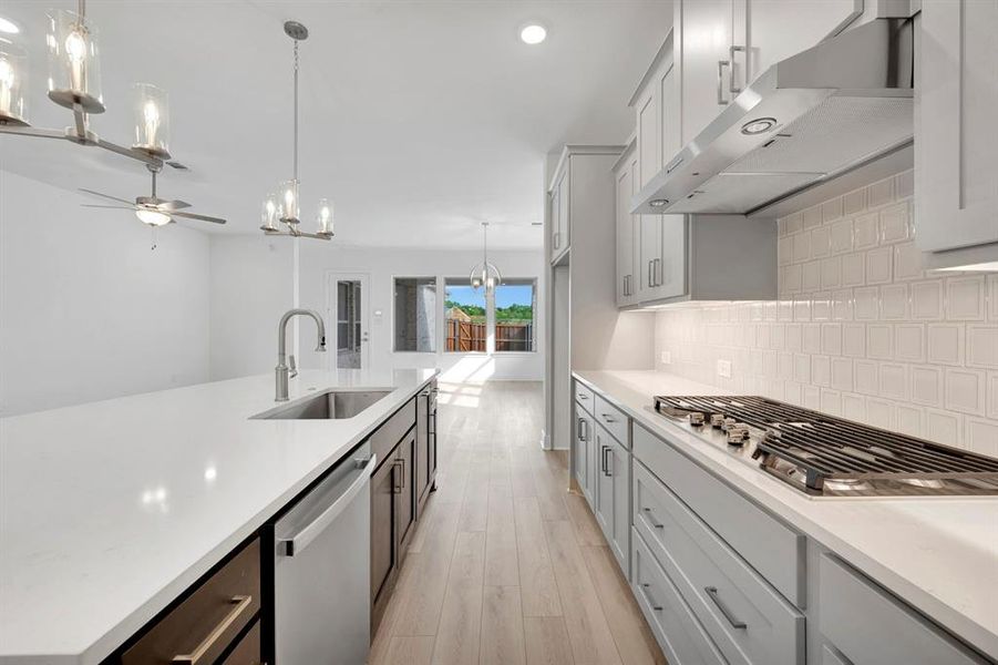 Kitchen featuring hanging lights, a ceiling fan, stainless steel appliances, light wood-style flooring, and light stone counters Kitchen featuring hanging lights, a ceiling fan, stainless steel appliances, light wood-style flooring, and light stone counters