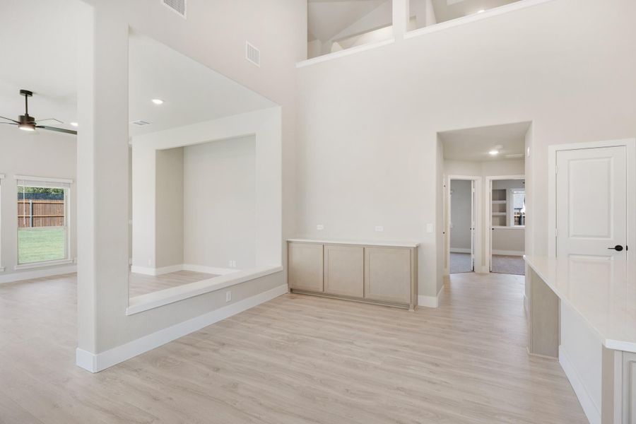 Open living area with two-story ceilings, light wood floors, and a built-in cabinet against white walls