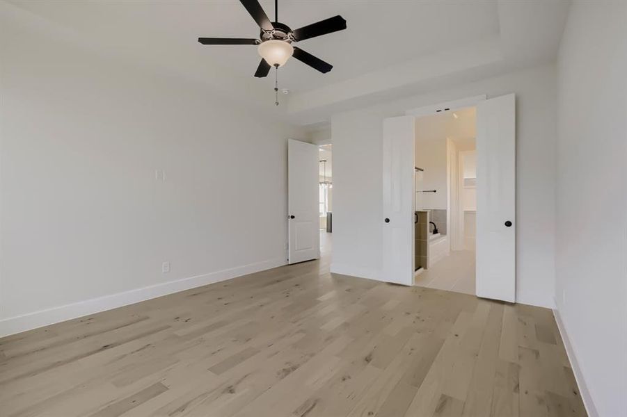 Spacious room with wood-finish flooring and a tray ceiling featuring a ceiling fan