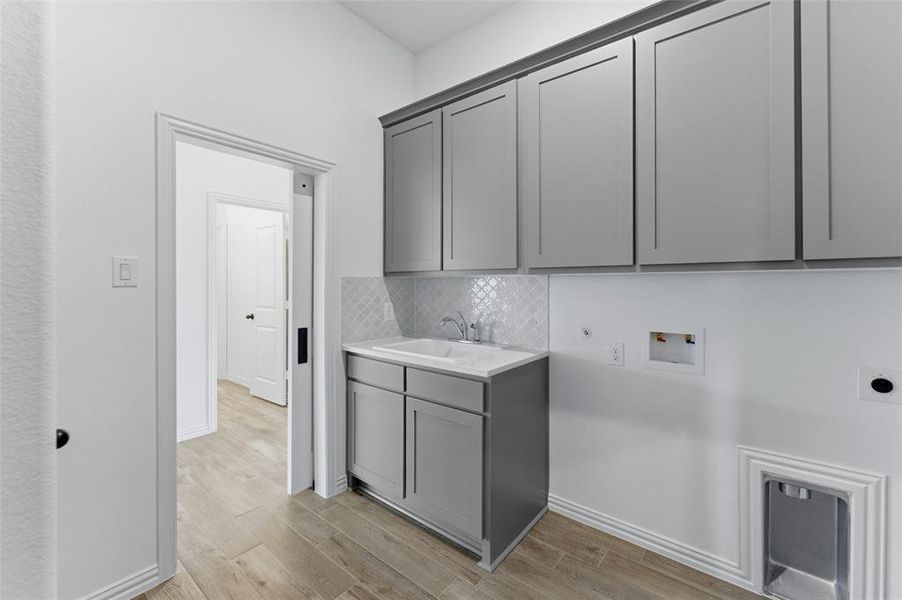 The utility room features light wood-look tile flooring, gray cabinetry with a sink, and a white tile backsplash