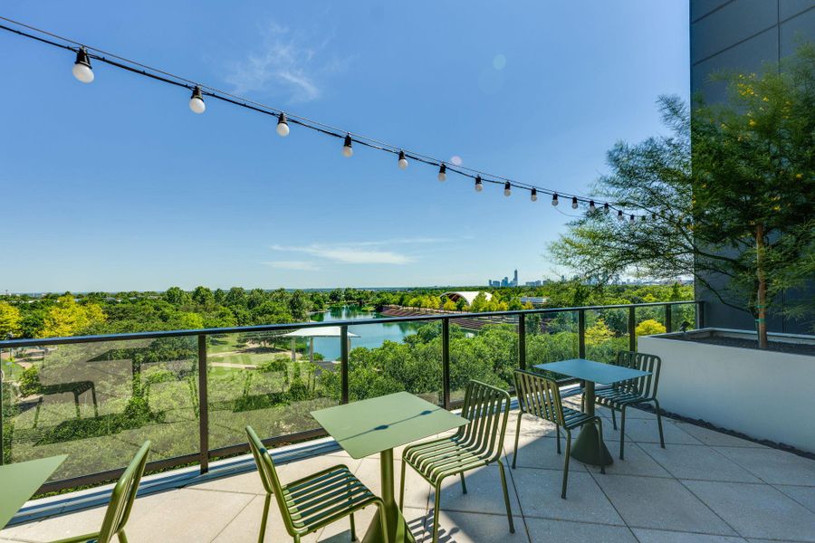 Outdoor patio featuring string lights, a clear glass railing, and a scenic view of a lake and green landscape