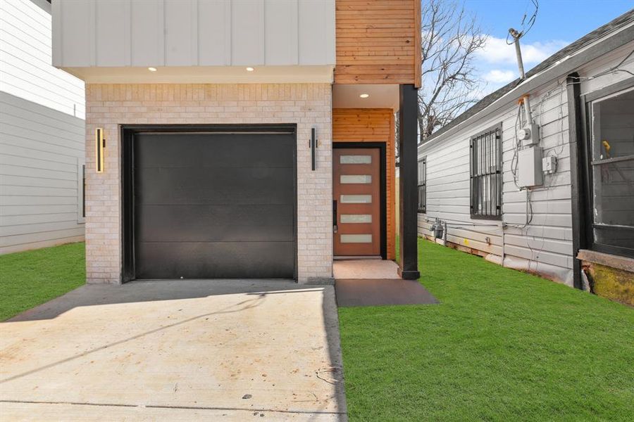 View of exterior entry featuring a garage, concrete driveway, brick siding, and a yard