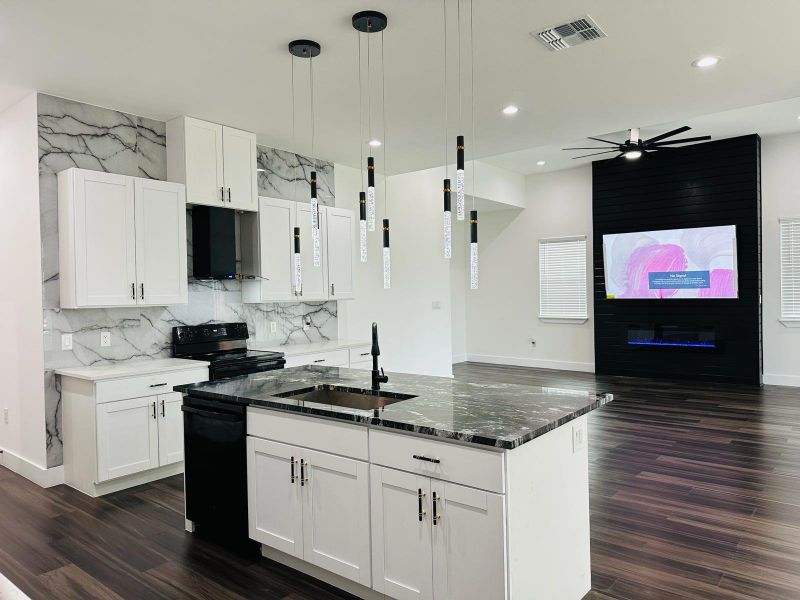 Kitchen with an island with sink, black appliances, a ceiling fan, pendant lighting, and dark stone countertops Kitchen with an island with sink, black appliances, a ceiling fan, pendant lighting, and dark stone countertops