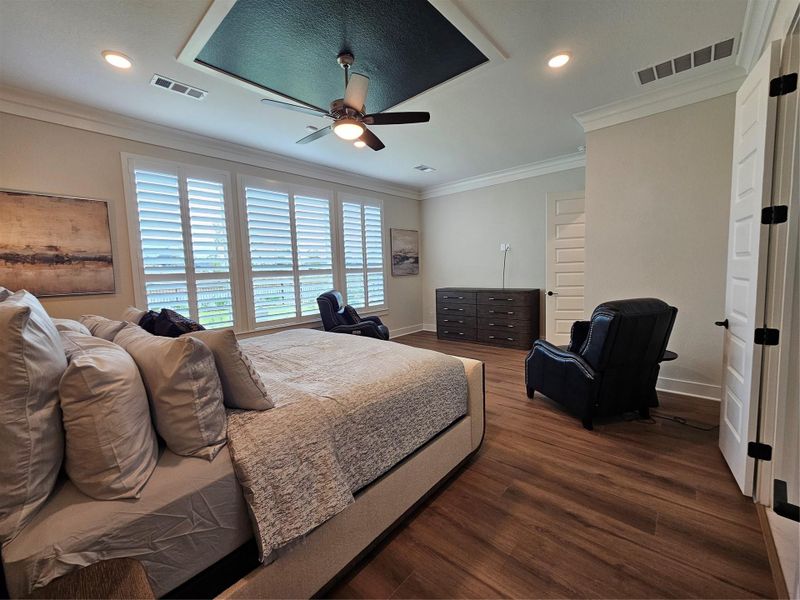 This spacious bedroom features hardwood floors, a stylish tray ceiling with a fan, and abundant natural light from large windows with shutters. It's furnished with a cozy bed and seating area, creating a comfortable and inviting atmosphere. This spacious bedroom features hardwood floors, a stylish tray ceiling with a fan, and abundant natural light from large windows with shutters. It's furnished with a cozy bed and seating area, creating a comfortable and inviting atmosphere.