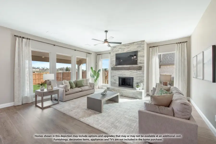 Living room with stone fireplace, ceiling fan, hardwood floors, and large windows with backyard views