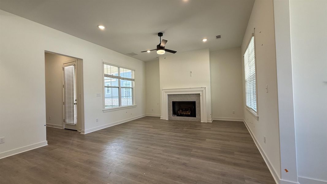 Unfurnished living room with ceiling fan, a tiled fireplace, dark wood-style floors, and recessed lighting