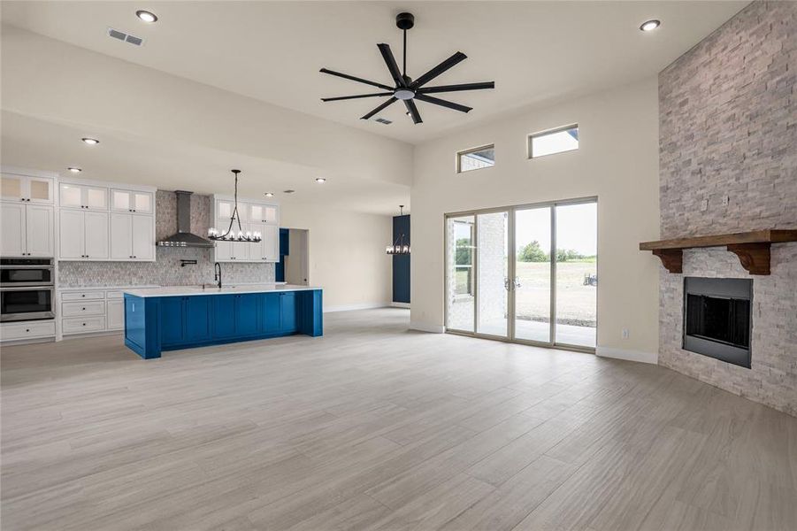 Unfurnished living room featuring a fireplace, a chandelier, a ceiling fan, light wood finished floors, and recessed lighting Unfurnished living room featuring a fireplace, a chandelier, a ceiling fan, light wood finished floors, and recessed lighting