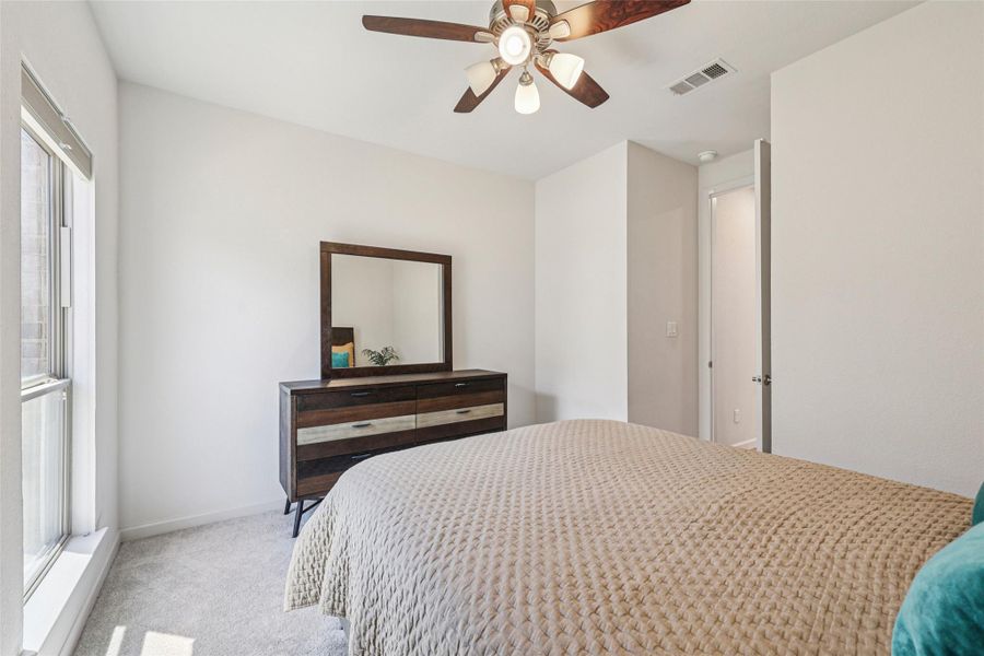 This room features a window providing natural light, a ceiling fan with integrated lighting, and light-colored carpeting