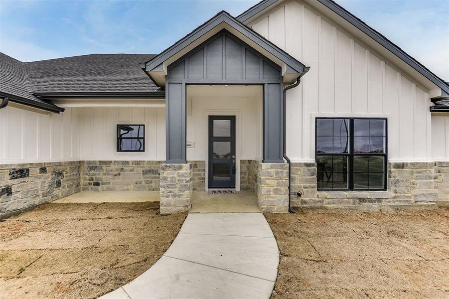 View of front of home with stone siding, a shingled roof, and board and batten siding