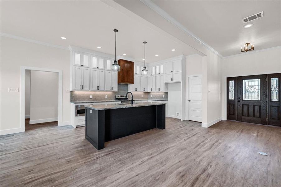 Kitchen featuring light hardwood / wood-style flooring, a kitchen island with sink, white cabinetry, and light stone countertops