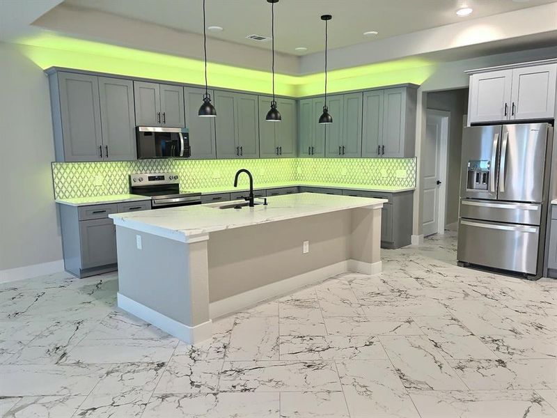 Kitchen with stainless steel appliances, tasteful backsplash, a kitchen island with sink, and light marble finish flooring