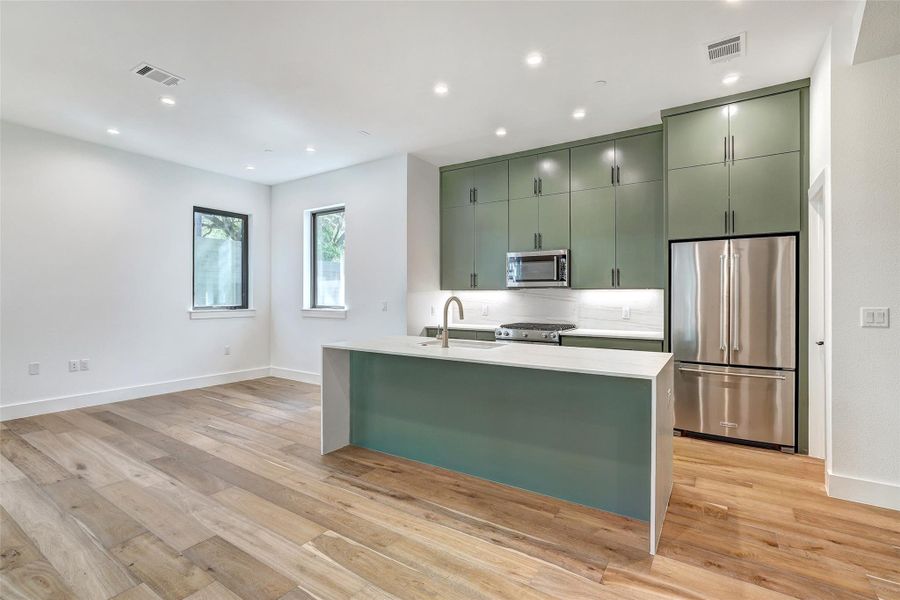 Kitchen with appliances with stainless steel finishes, green cabinets, a sink, light countertops, and recessed lighting