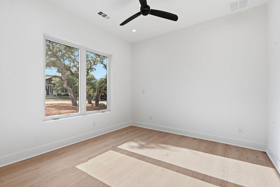 Sunlight streams through wide windows onto light wood flooring in this minimalist modern bedroom.